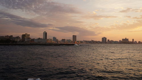 Sea by cityscape against sky during sunset