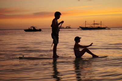 Silhouette people on sea against sky during sunset