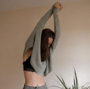 Midsection of woman with arms raised against wall