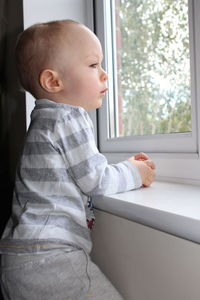 Side view of cute baby boy looking through window