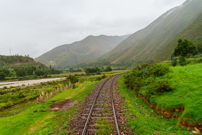 Empty railroad track amidst grassy field leading towards mountains