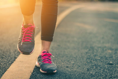 Low section of woman wearing sports shoes while walking on road