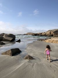 Rear view of girl walking on beach against sky