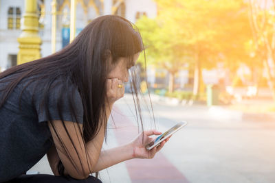 Side view of young woman using mobile phone outdoors