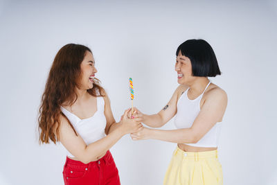 Lesbian couple holding lollipop against white background