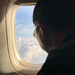 Close-up of man looking through airplane window