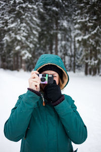 Young man photographing while standing on snow covered land