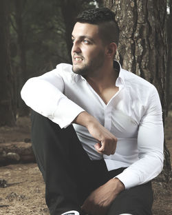 Thoughtful young man sitting against tree trunk