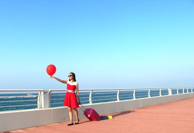 Woman with red umbrella against sea against clear sky