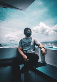 Young man sitting by sea against sky