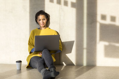 Portrait of smiling young woman sitting on the floor using laptop