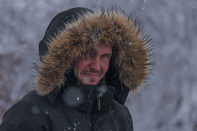 Portrait of man wearing fur coat standing outdoors during snowfall