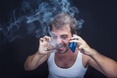 Close-up portrait of man smoking over black background