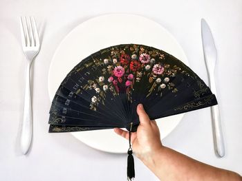 Close-up of hand holding hand fan over place setting on table