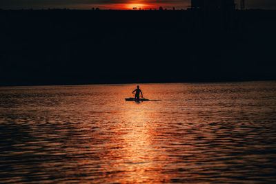 Silhouette person in sea against sky during sunset