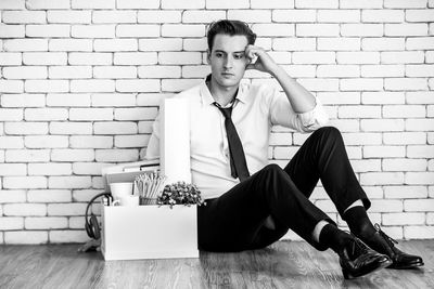 Portrait of young man sitting against wall