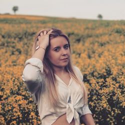 Portrait of beautiful woman with hand in hair standing amidst plants on field