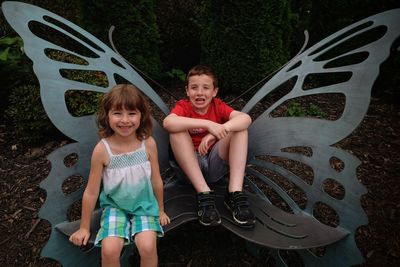 Portrait of siblings sitting on wing shaped chair