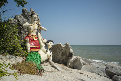 Side view of woman sitting on rock at beach