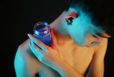 Shirtless man holding drinking glass on shoulder against black background