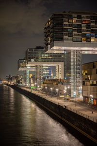 Illuminated buildings by river against sky in city at night