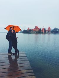 Portrait of embracing while standing on pier over lake during monsoon