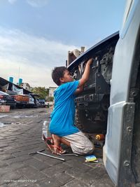 Side view of boy on car against sky