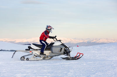 Side view of man riding snowmobile on snow covered landscape against sky