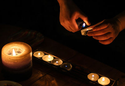 Midsection of person holding illuminated candles on table