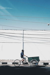 Man riding bicycle in city against blue sky