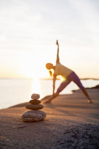 Woman practices yoga on lakeshore with focus on stack of stones