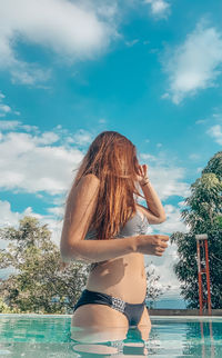 Woman standing by swimming pool against sky