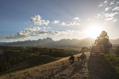 Rear view of friends sitting on field against sky