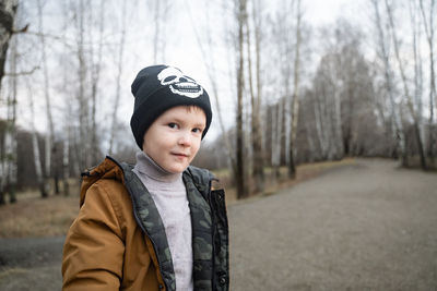 Portrait of boy standing against bare trees during winter