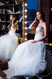 Beautiful bride wearing wedding dress while sitting by mirror