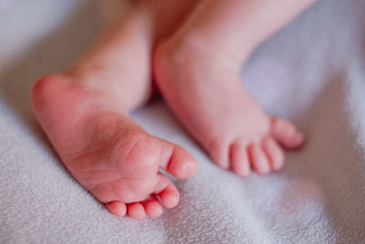 High angle of closeup feet of unrecognizable tranquil infant with pink skin and tiny toes against blurred white bed sheet at home