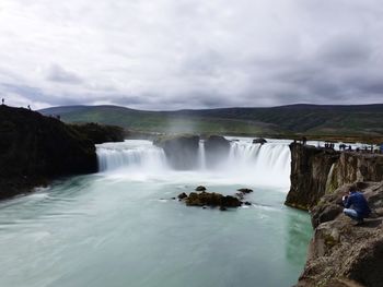 Scenic view of waterfall against cloudy sky