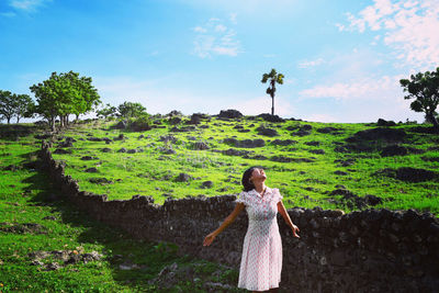 Woman standing on field by trees against sky