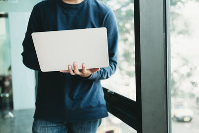 Midsection of man holding mobile phone while standing on window