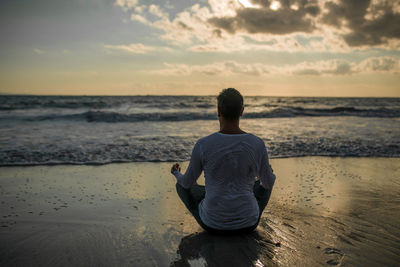 Rear view of man meditating at beach during sunset