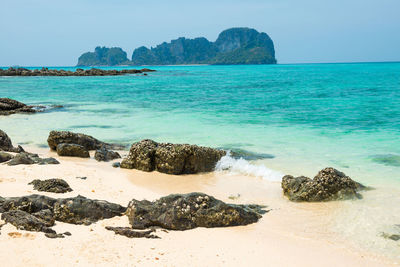 Tropical sea landscape with rocks at sand beach and rocky island at horizon