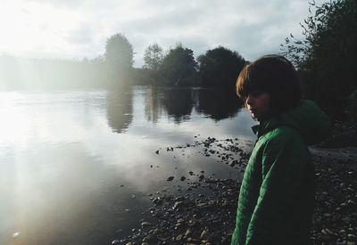 Side view of woman standing by lake against sky