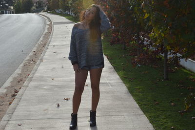 Portrait of young woman with hand in hair standing on footpath by road