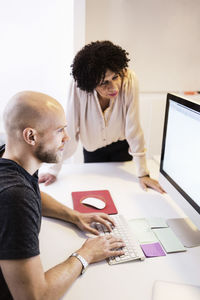 Side view of businessman using computer while colleague looking at it in office