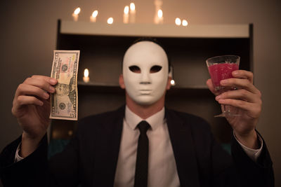 Man wearing mask while holding drink and currency at hotel