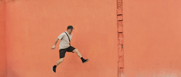 Mature asian man in casual clothes running through air over of bright orange wall background.