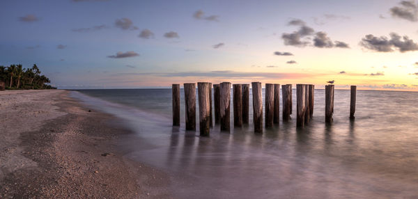 Wooden posts on beach against sky during sunset