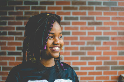 Close-up of smiling young woman standing against brick wall