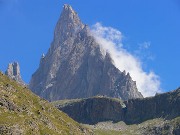 Low angle view of rocky mountains against clear blue sky on sunny day