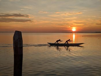 Silhouette people in sea against sky during sunset